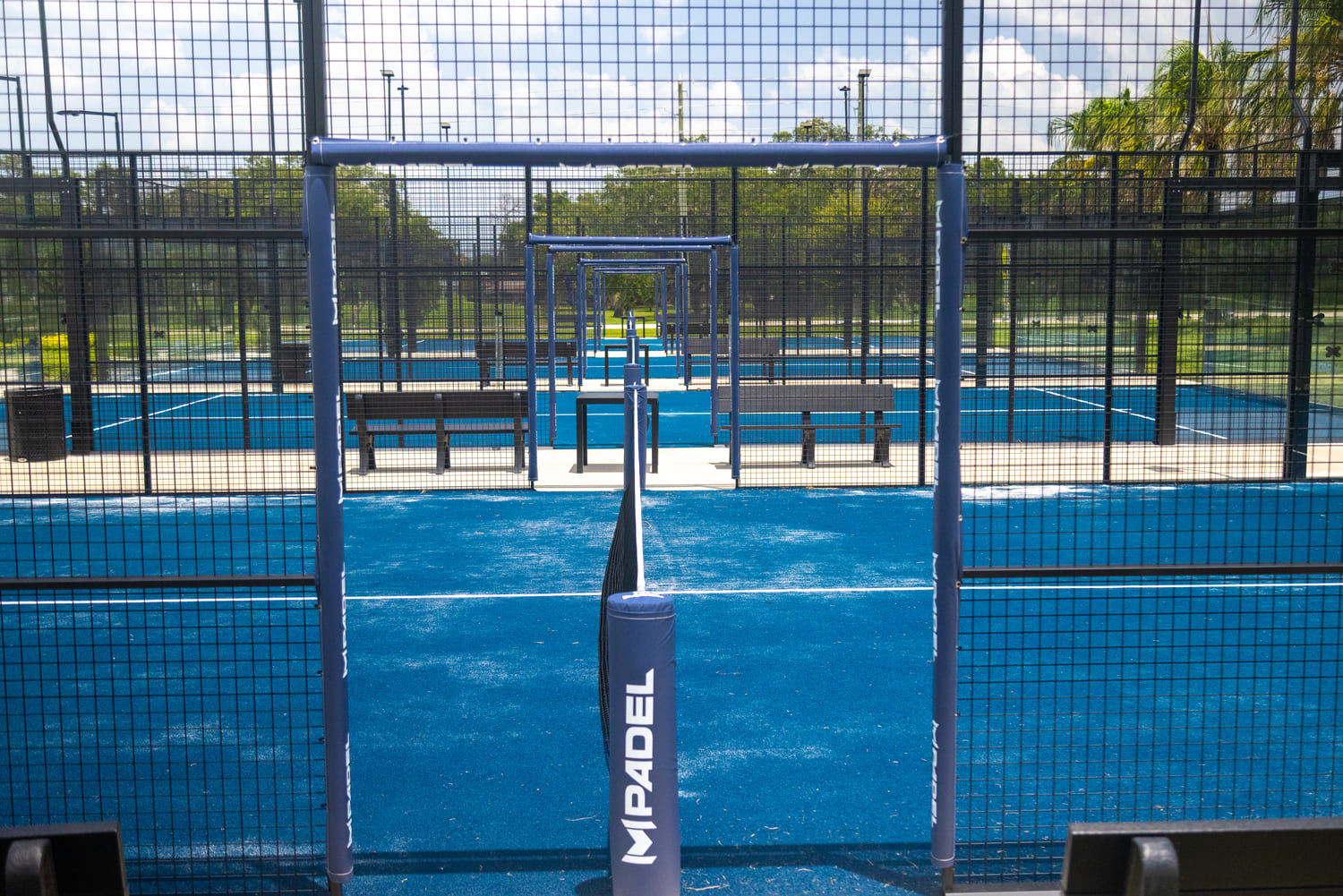 Multiple blue outdoor padel courts with nets, benches, and fencing at M Padel Zephyrhills.